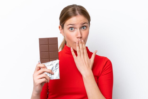 Young caucasian woman isolé sur fond blanc en prenant une tablette de chocolat et surpris