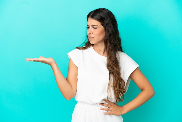 Young caucasian woman isolé sur fond bleu holding copyspace avec des doutes