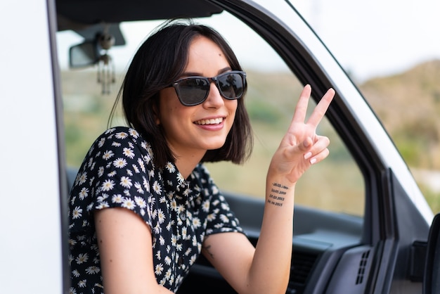 Young caucasian woman smiling et montrant le signe de la victoire avec un visage joyeux dans une camionnette à l'extérieur