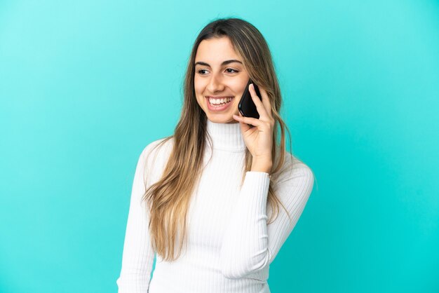 Young caucasian woman using mobile phone isolé sur fond bleu à côté