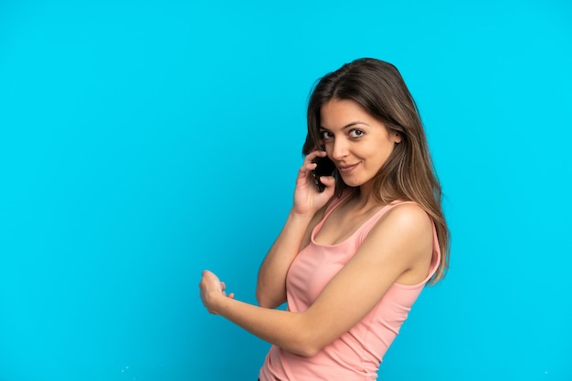 Young caucasian woman using mobile phone isolé sur fond bleu pointant vers l'arrière