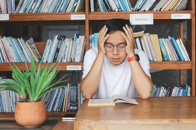 Young College Student Man lisant un livre dans la bibliothèque au sérieux