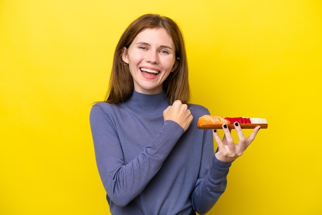 Young English woman holding sashimi isolé sur fond jaune célébrant une victoire