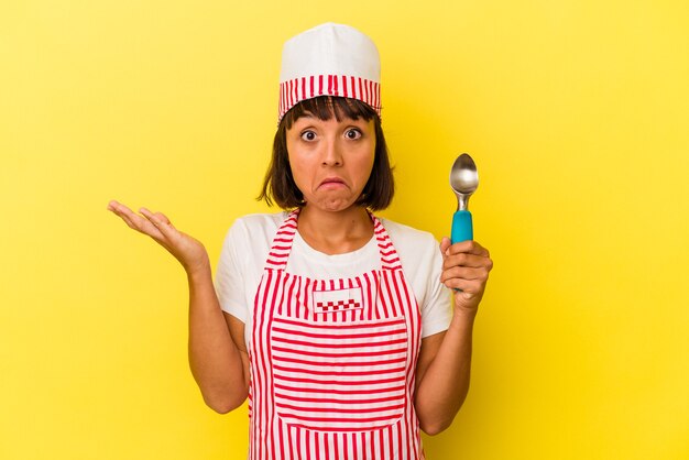 Young mixed race ice cream maker woman holding an ice cream scoop isolé sur fond jaune