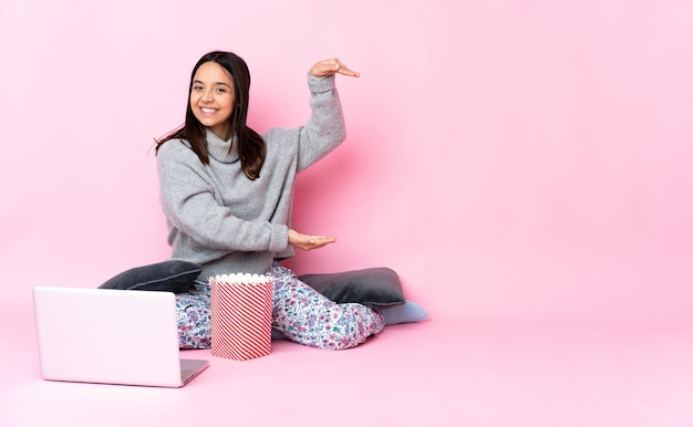 Young mixed race woman eating popcorn tout en regardant un film sur l'ordinateur portable holding copyspace pour insérer une annonce