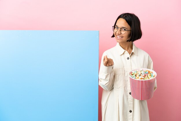 Young mixed race woman holding pop-corn avec une grande bannière sur fond isolé faisant de l'argent geste