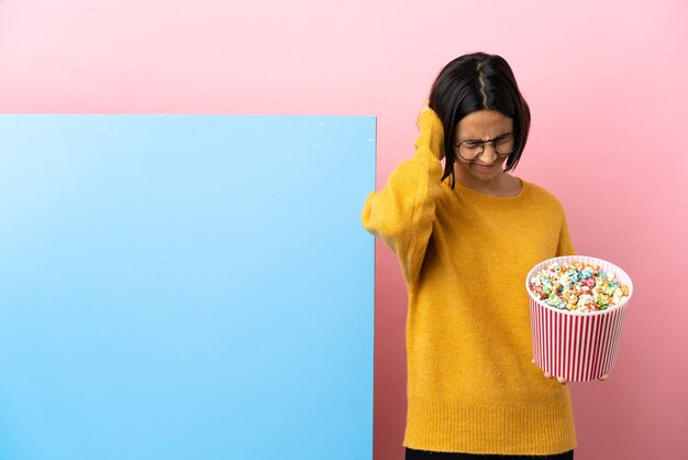 Young mixed race woman holding pop-corn avec une grande bannière sur fond isolé frustré et couvrant les oreilles