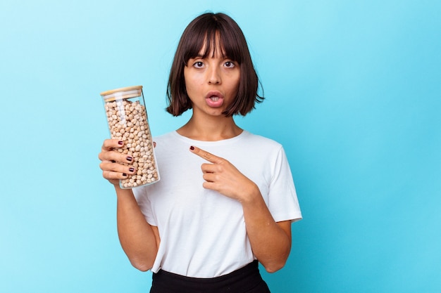 Young mixed race woman holding pot de pois chiches isolé sur fond blanc pointant vers le côté