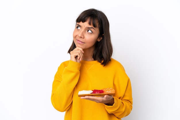 Young mixed race woman holding sashimi isolé sur fond blanc ayant des doutes