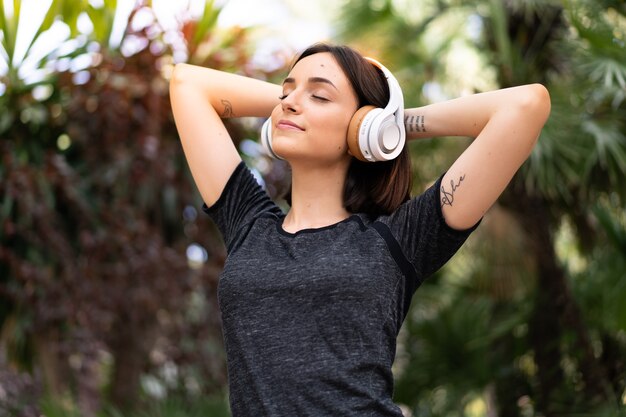 Young sport caucasian woman écouter de la musique avec des écouteurs à l'extérieur dans un parc