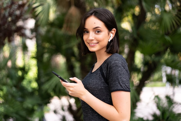 Young sport caucasian woman envoyer un message ou un e-mail avec le mobile à l'extérieur dans un parc