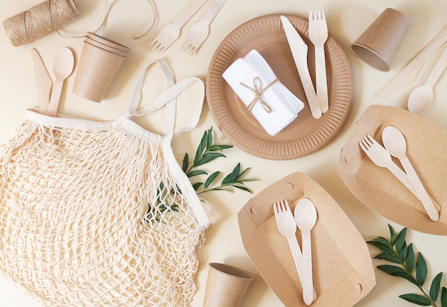 Zéro déchet, vie sans plastique et respectueuse de l'environnement. Vaisselle jetable en papier, couverts en bois et sac en filet de coton vue de dessus sur table beige