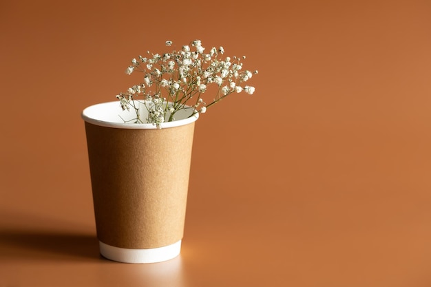 Zero Waste Lifestyle Craft Gobelet marron jetable avec couvercle en plastique blanc et un brin de fleurs séchées sur fond marron espace de copie isolé