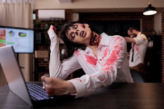 Zombie cruel d'horreur utilisant un ordinateur portable au bureau, un cadavre de mort-vivant essayant de travailler sur un ordinateur dans un bureau de démarrage. Cerveau agressif effrayant mangeant un monstre à la recherche d'un danger terrifiant et horrible, sinistre.