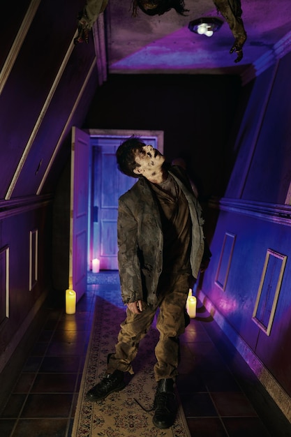 Zombie laid marchant dans le hall de la maison d'horreur illuminée au néon voyant cruel, personnage au plafond