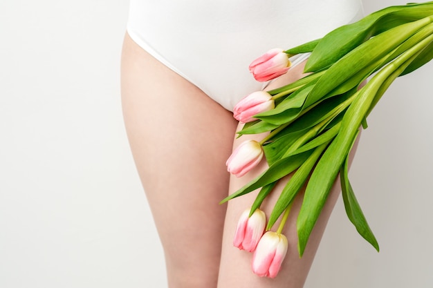 Zone de bikini d'une jeune femme portant un sous-vêtement blanc avec des tulipes roses sur fond blanc