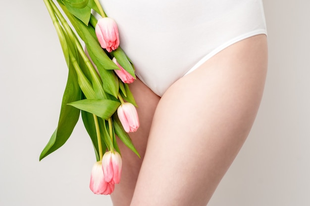 Zone de bikini d'une jeune femme portant un sous-vêtement blanc avec des tulipes roses sur fond blanc