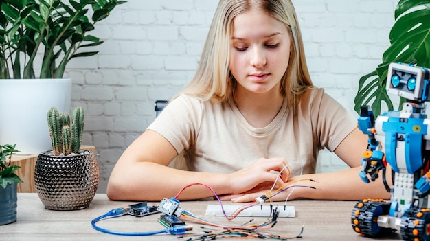 A blonde teen girl plugging cables to sensor chips while learning arduino coding and robotics
