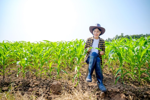 a female asian farmer wearing a striped top and hat is sitting happily watching the corn crop