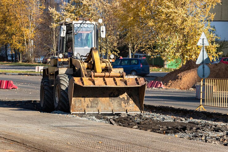 Foto a heavy front loader transports earth in a bucket and grades the road. road repair in the center of a modern city in autumn. heavy construction machinery for moving soil.