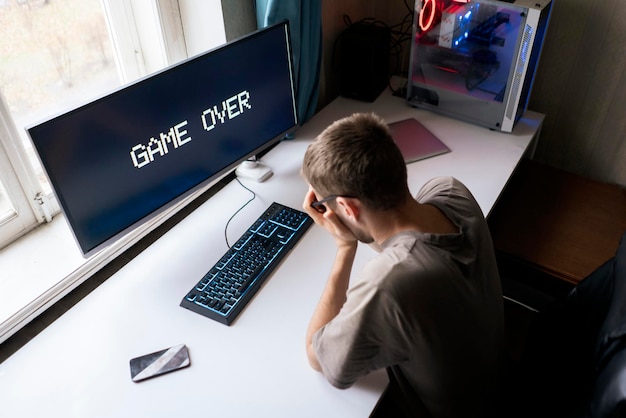 A male gamer loosing a video game, game over text on the screen