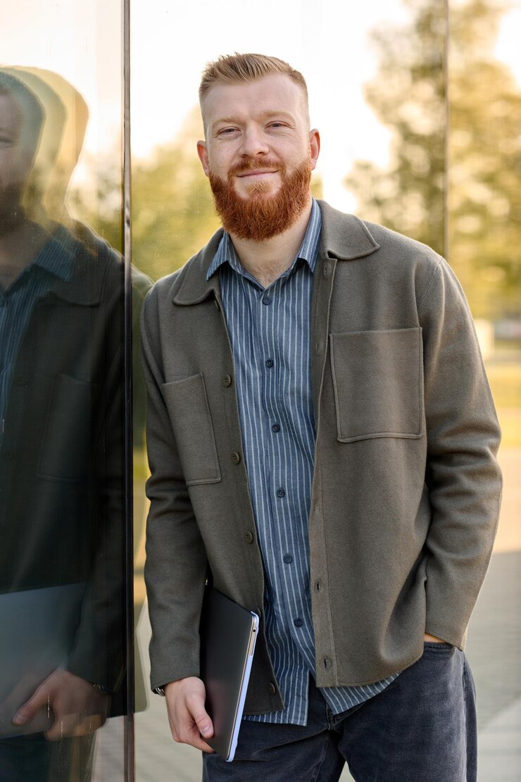 Foto a man with a red beard dressed in a shirt and jacket stands at the entrance to a business center with a laptop