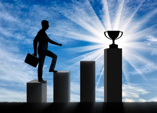 A silhouette of a businessman going up the steps to the trophy. The business concept of the career ladder