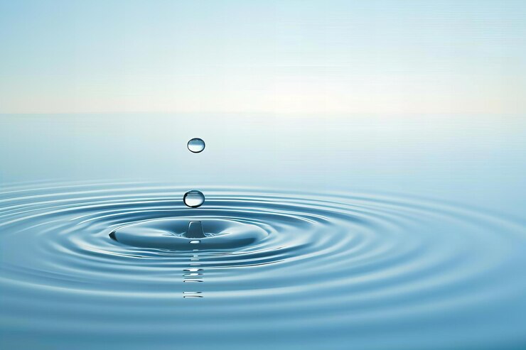 A single water droplet falling into the calm blue waters creating ripples that spread out from its