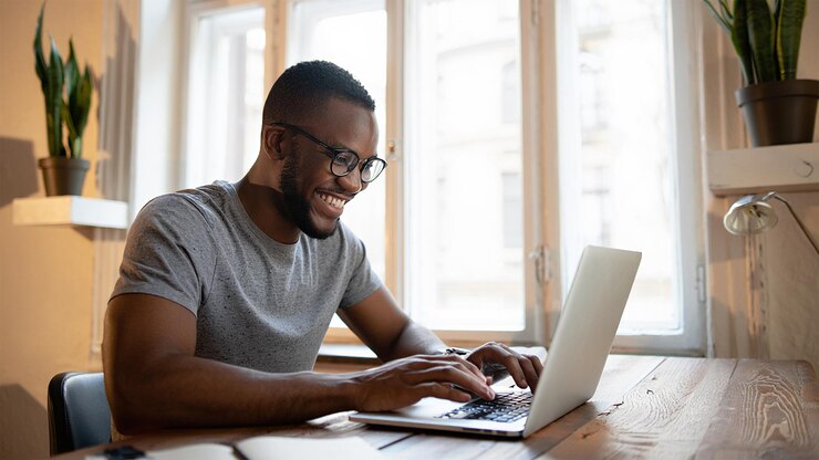 A smiling stylish entrepreneur intently works on their laptop near a large window radiating focus