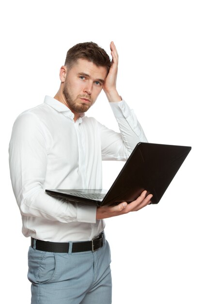 A young man with a laptop in his hands has problems with his computer, holds his head and looks into the frame. The figure is isolated on a white background.