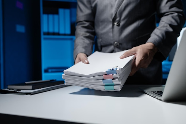 An employee held a large pile of documents in his hand Large piles of work documents on desks are being sorted by employees Important documents are stacked