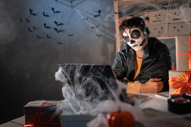 Arab man business owner wears white clay skull professional makeup in home office with headset sitting bored Festive decorated office halloween sale concept Banner