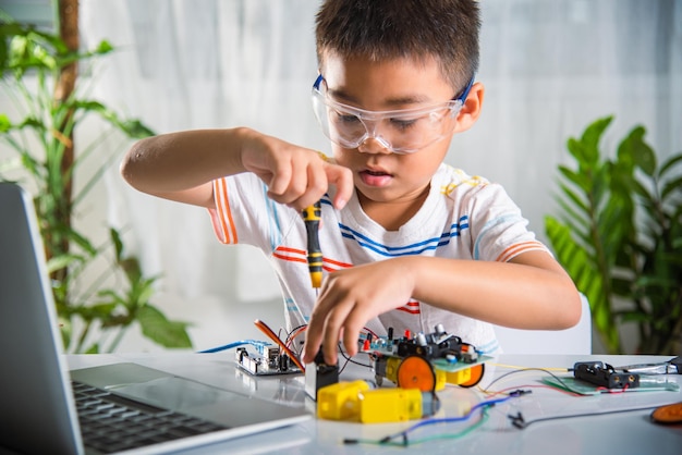 Asian kid boy assembling the Arduino robot car homework project at home