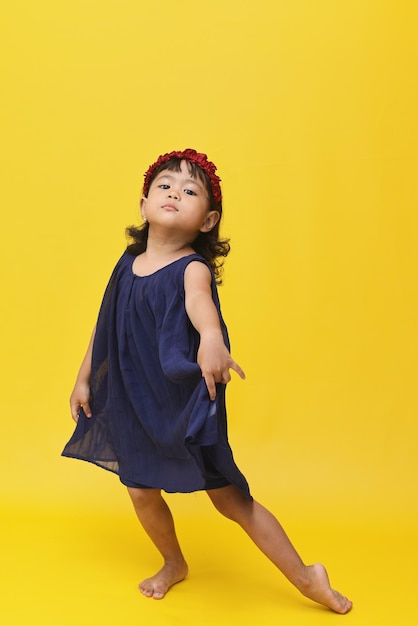 Attractive Asian little girl dancing with elegant face isolated on yellow background