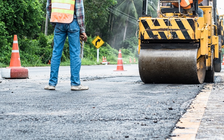 Foto back view standing engineer and small asphalt roller in on duty repairing repairing asphalt road. workers on a road construction, industry and teamwork.