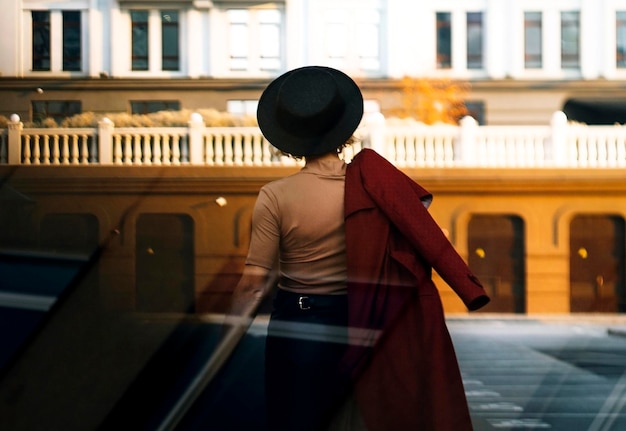 Back view woman walking on city street at sunset wearing hat and coat