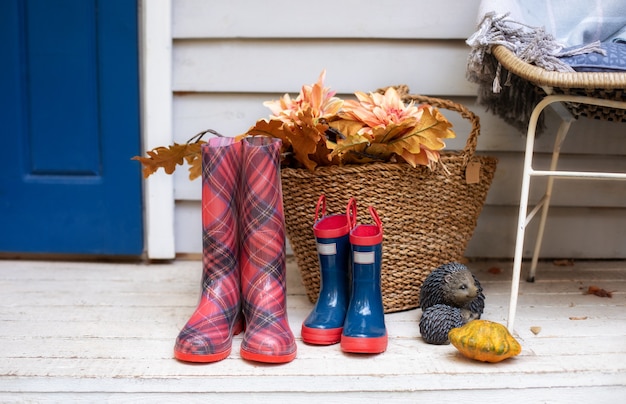 basket with leaves, pumpkin and rubber boot in yard. checkered and blue rain boots of house on porch