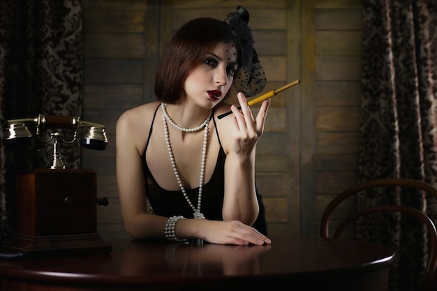 beautiful 1930s girl smokes a cigarette at the table