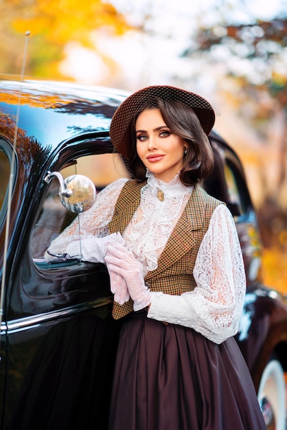 beautiful female in vintage  dress, lace blouse and hat with veil standing near retro brown car