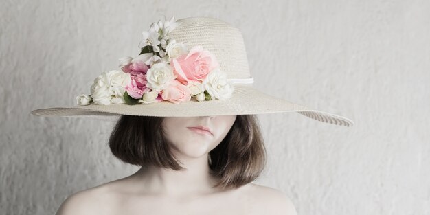 Beautiful girl in hat with flowers on gray background