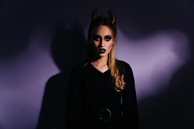 Beautiful witch with dark makeup posing in studio Attractive woman in halloween costume expressing interest
