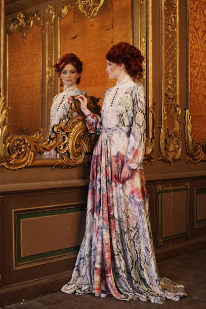 Beautiful woman standing in the palace room with mirror. 