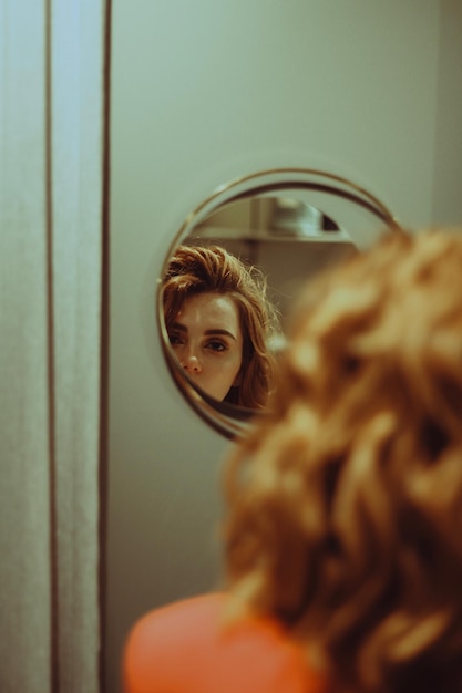 Beautiful young woman looking in mirror at home
