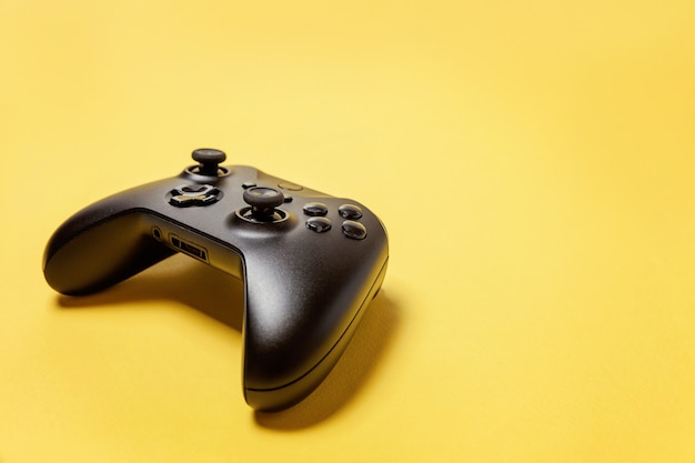 Black joystick gamepad, game console on yellow background. Computer gaming videogame control confrontation concept