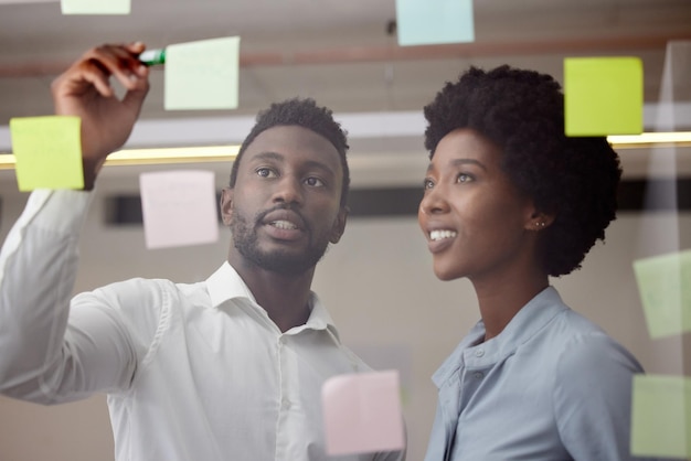 Black people writing and thinking of idea on post it wall for brainstorming meeting pitch Innovation strategy and development of business goal with professional corporate planning team