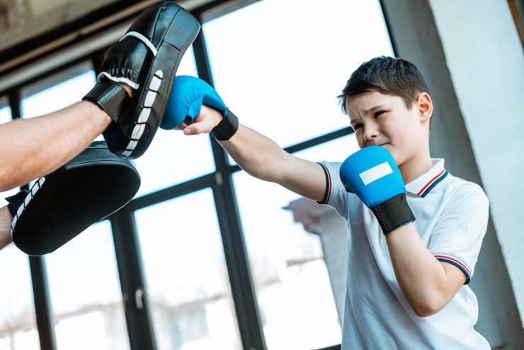 Foto boy in boxing gloves working out with coach at gym