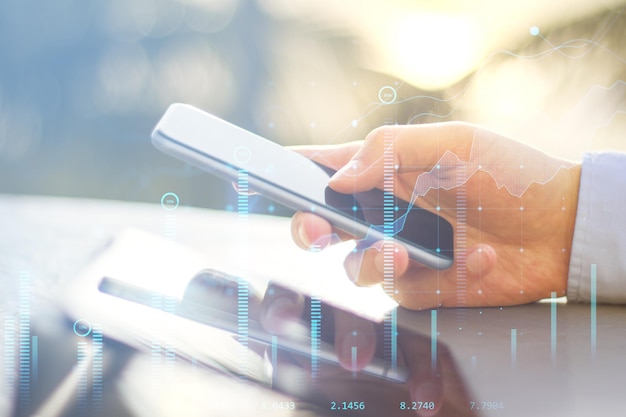 close up of businessman hand at desktop using smartphone with creative glowing business chart on blurry background growth sales and market concept double exposure