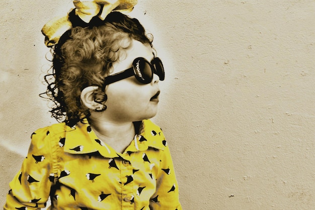 Close-up of girl wearing sunglasses against wall