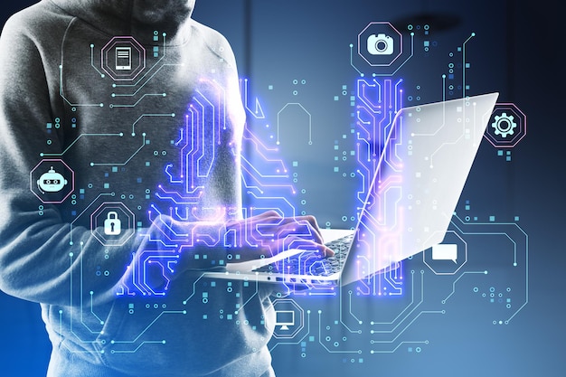Close up of hacker in hoodie using laptop with glowing blue AI hologram on blurry background Artificial intelligence technology and innovation concept