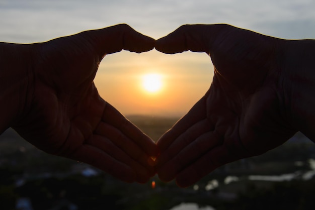 Close-up of hand against sun during sunset